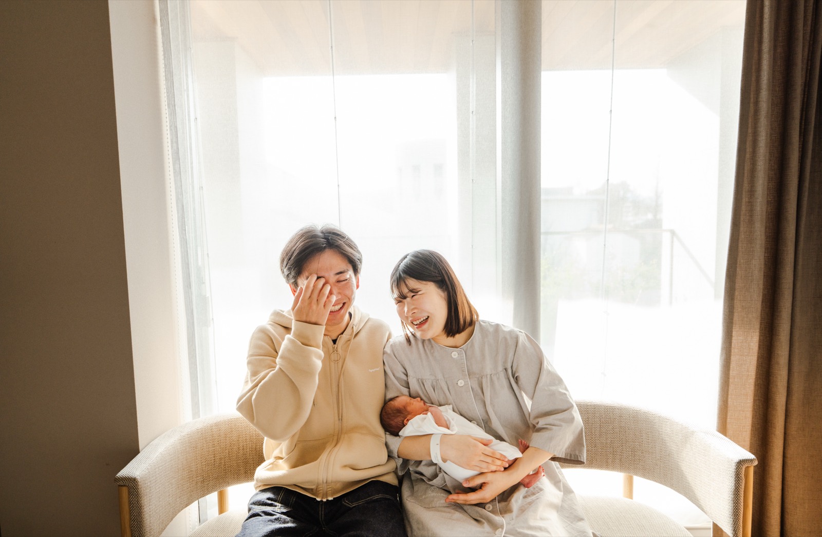 窓辺で赤ちゃんを抱くご家族の写真