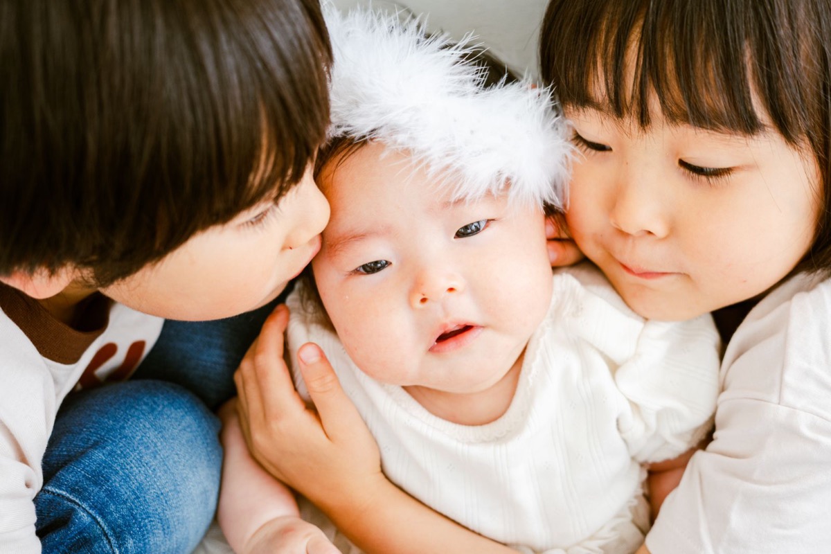 赤ちゃんに頬を寄せる兄姉の写真