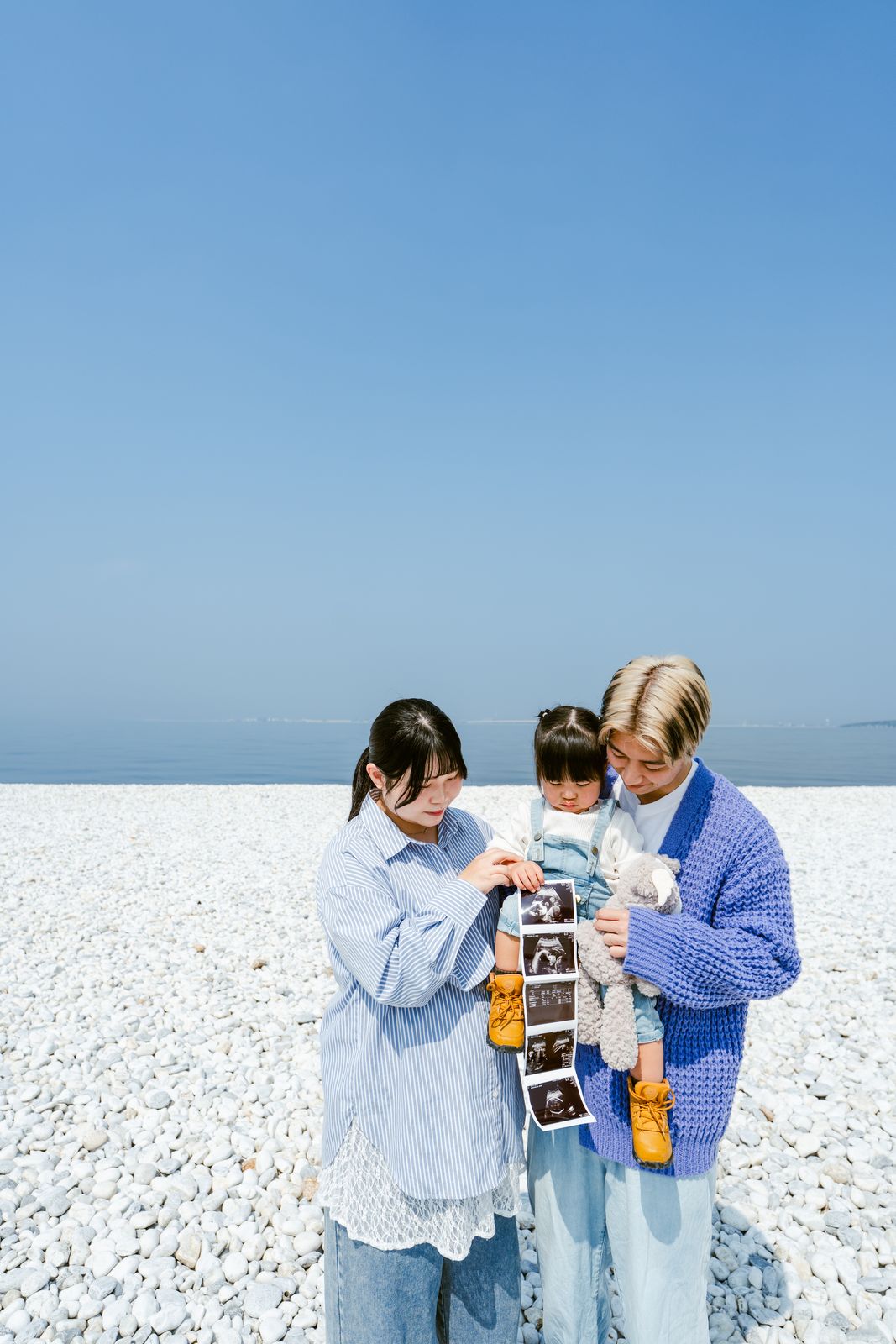 海辺でエコー写真を眺めるご家族のマタニティ写真