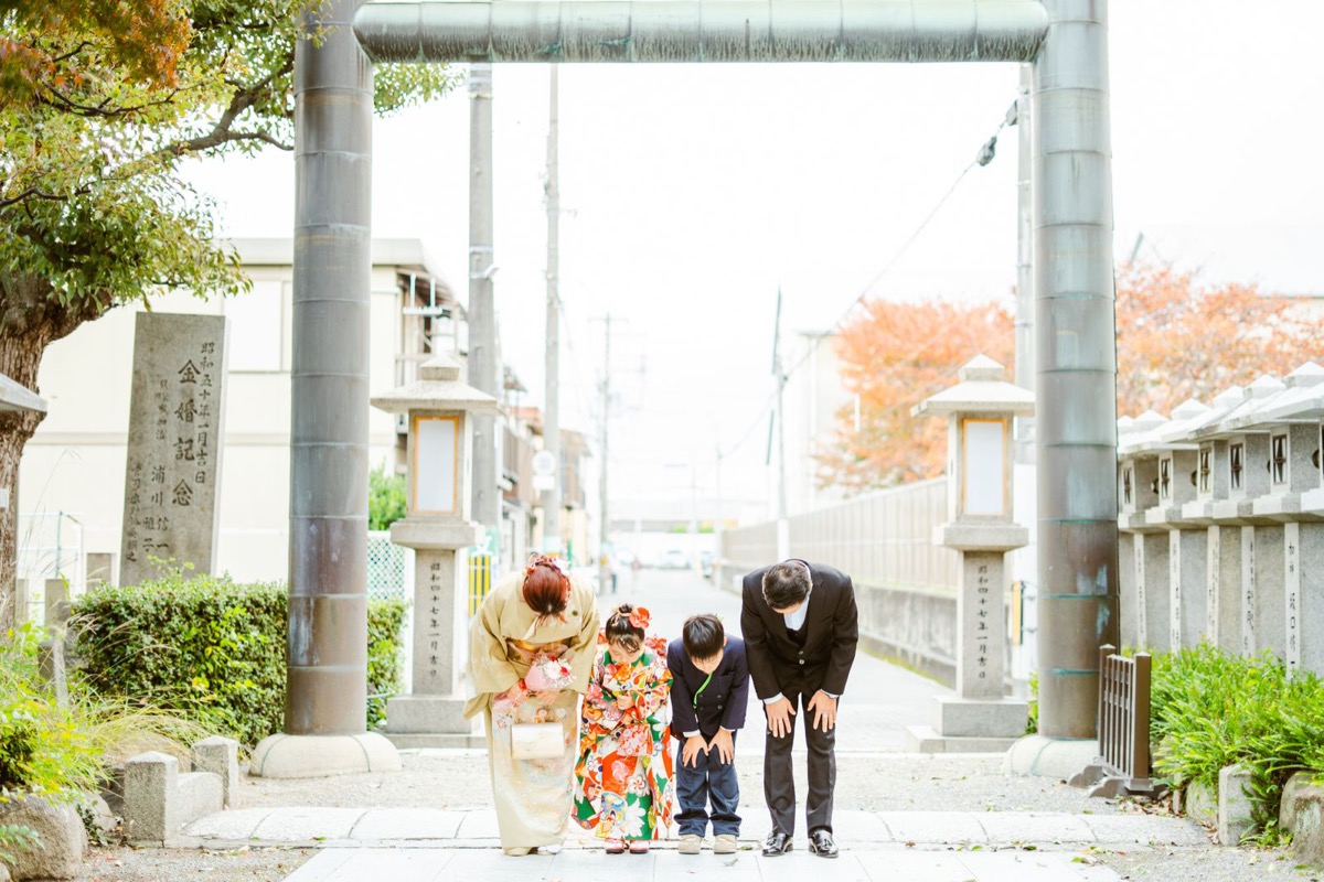 鳥居の前でおじぎをする七五三のご家族の写真